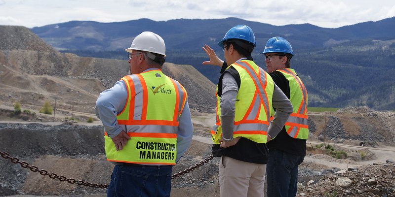 Three men wearing safety equipment on mine site with mountains in the background